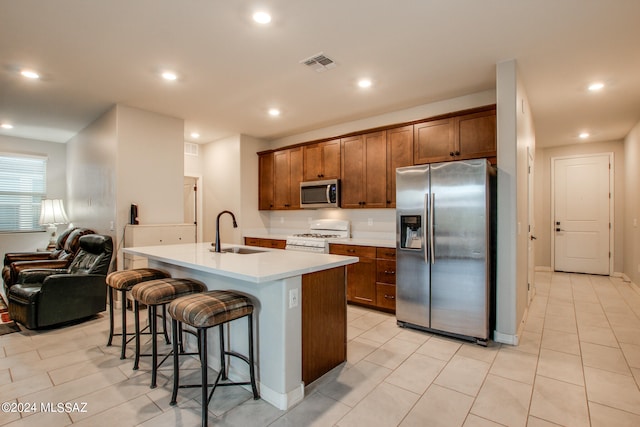 kitchen with appliances with stainless steel finishes, light tile patterned floors, sink, and a kitchen island with sink