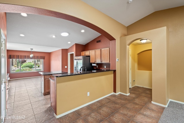 kitchen with kitchen peninsula, dark tile patterned flooring, vaulted ceiling, and stainless steel refrigerator with ice dispenser