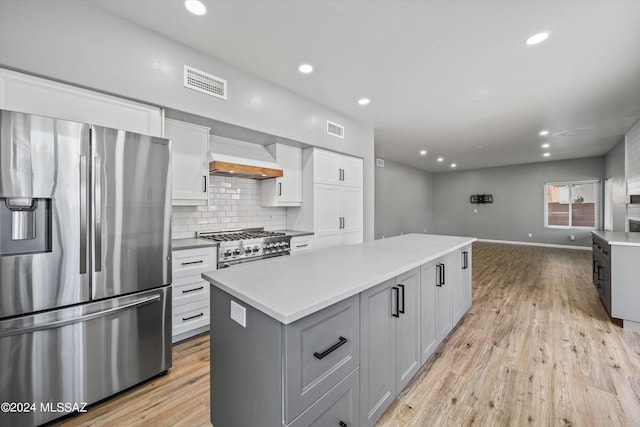 kitchen with appliances with stainless steel finishes, custom exhaust hood, light wood-type flooring, white cabinetry, and a center island