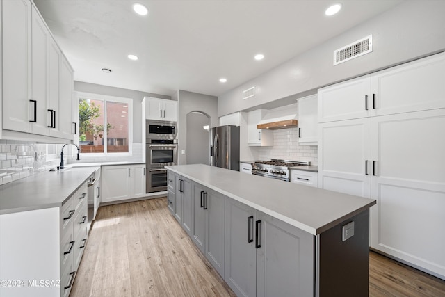 kitchen featuring white cabinets, appliances with stainless steel finishes, a kitchen island, light hardwood / wood-style flooring, and custom range hood