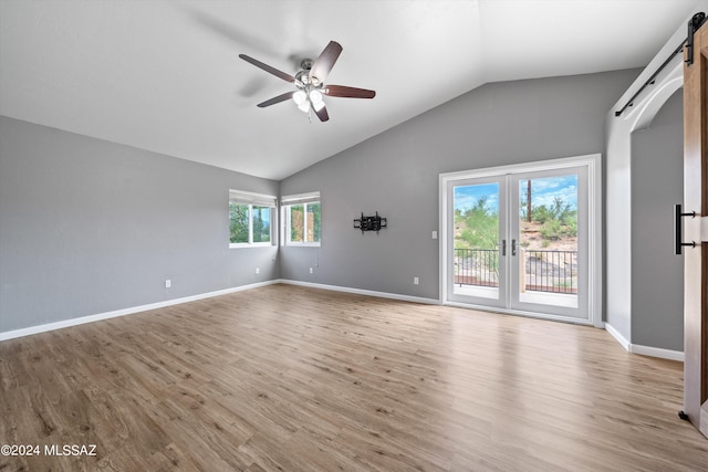 empty room with light hardwood / wood-style flooring, a wealth of natural light, lofted ceiling, and a barn door