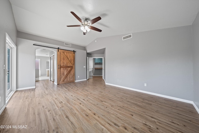 unfurnished living room featuring light hardwood / wood-style floors, ceiling fan, a barn door, and vaulted ceiling