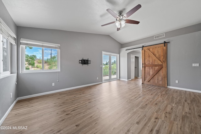 empty room featuring a healthy amount of sunlight, a barn door, light hardwood / wood-style floors, and lofted ceiling