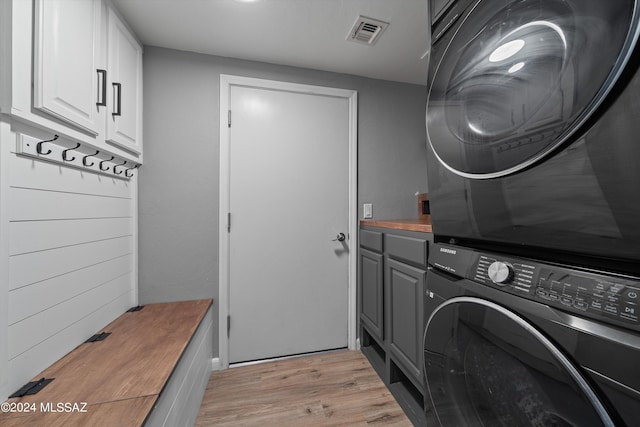 washroom with cabinets, light wood-type flooring, and stacked washer and dryer