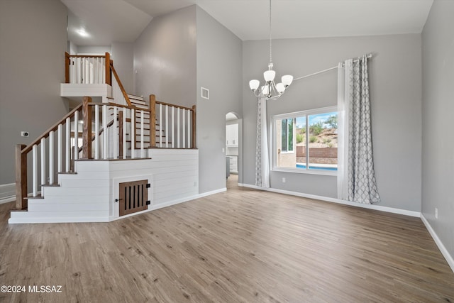 unfurnished living room with hardwood / wood-style floors, a chandelier, and high vaulted ceiling