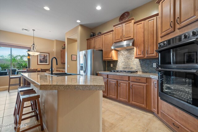 kitchen with light tile patterned floors, an island with sink, stainless steel appliances, decorative backsplash, and pendant lighting