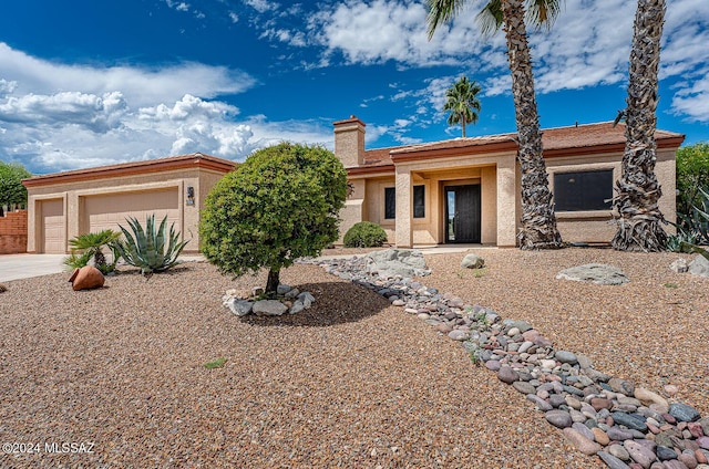 view of front of property featuring a garage, driveway, a chimney, and stucco siding