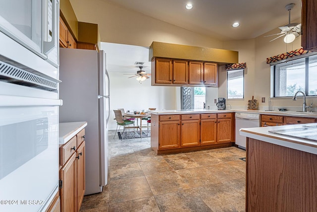 kitchen featuring a peninsula, white appliances, brown cabinetry, and a sink