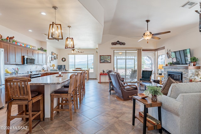 interior space featuring ceiling fan with notable chandelier, a stone fireplace, and tile patterned floors