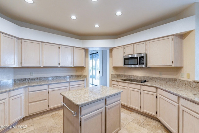 kitchen with black electric stovetop, light stone counters, and a kitchen island