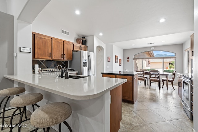 kitchen with sink, a breakfast bar area, a center island with sink, stainless steel appliances, and decorative backsplash