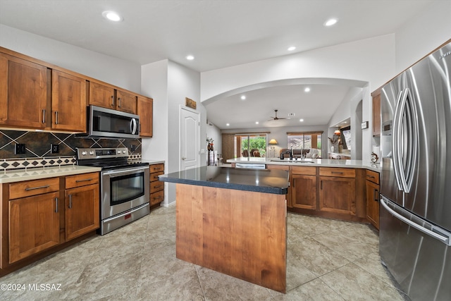 kitchen with sink, vaulted ceiling, a kitchen island, stainless steel appliances, and decorative backsplash