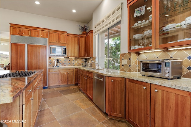 kitchen featuring tasteful backsplash, light stone counters, stainless steel appliances, and sink