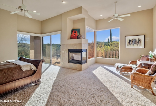 living room featuring light colored carpet, ceiling fan, a towering ceiling, and a tile fireplace