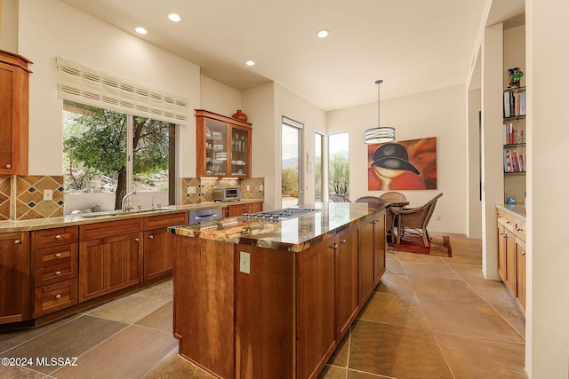 kitchen with hanging light fixtures, tasteful backsplash, a center island, light stone countertops, and sink