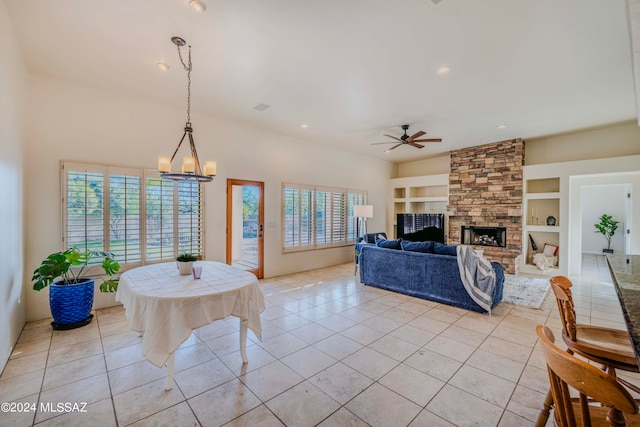 tiled living room featuring a wealth of natural light, a fireplace, ceiling fan with notable chandelier, and built in features