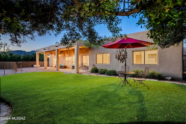 back house at dusk featuring a patio and a lawn