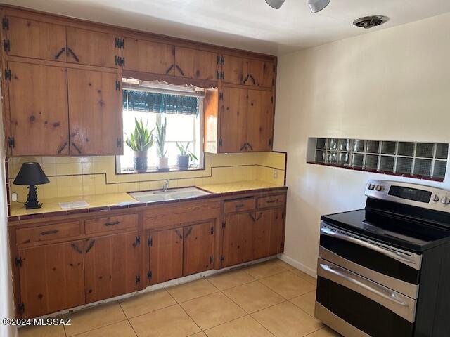 kitchen featuring decorative backsplash, tile counters, stainless steel electric range, sink, and light tile patterned flooring