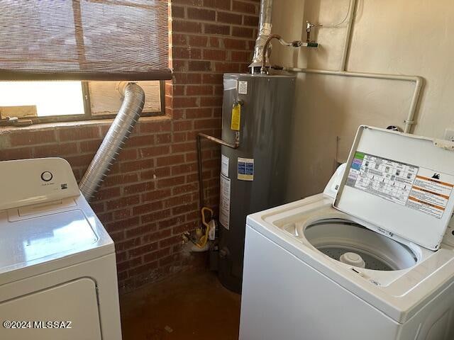 clothes washing area featuring washing machine and clothes dryer, brick wall, and water heater