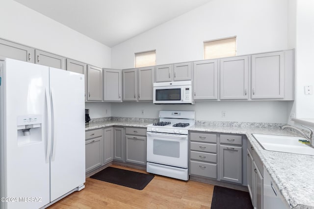 kitchen with gray cabinets, lofted ceiling, sink, light wood-type flooring, and white appliances