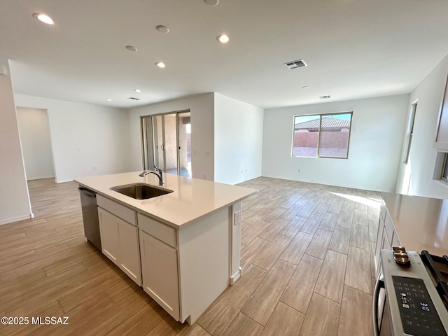 kitchen featuring sink, a kitchen island with sink, white cabinetry, stove, and stainless steel dishwasher