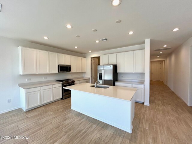 kitchen with light hardwood / wood-style flooring, an island with sink, white cabinets, and appliances with stainless steel finishes