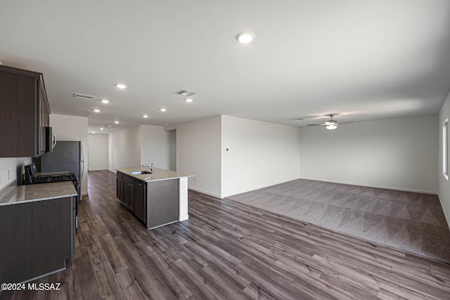 kitchen featuring dark carpet, an island with sink, ceiling fan, sink, and dark brown cabinetry