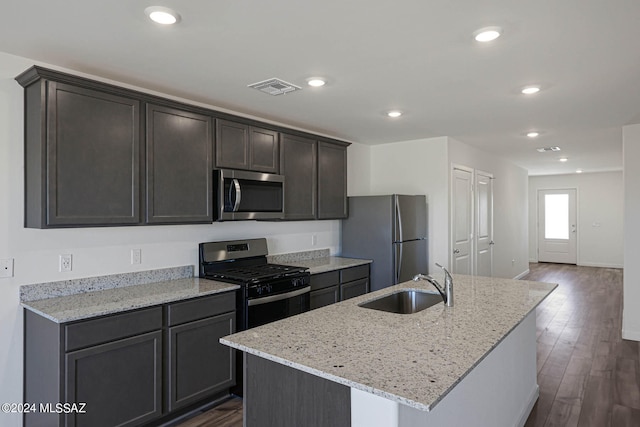 kitchen featuring dark hardwood / wood-style flooring, stainless steel appliances, an island with sink, light stone counters, and sink