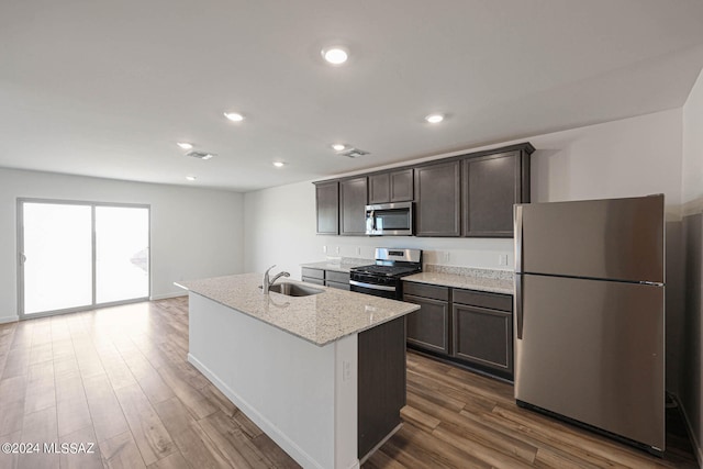 kitchen featuring appliances with stainless steel finishes, light stone countertops, wood-type flooring, a center island with sink, and sink