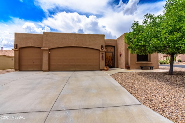pueblo-style house with an attached garage, driveway, and stucco siding
