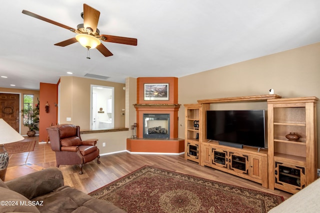 living area with wood finished floors, visible vents, a ceiling fan, baseboards, and a glass covered fireplace