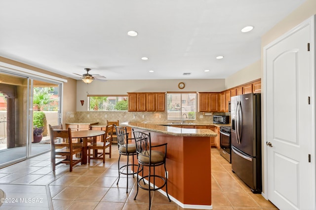 kitchen with light tile patterned flooring, decorative backsplash, a kitchen bar, stainless steel refrigerator with ice dispenser, and ceiling fan