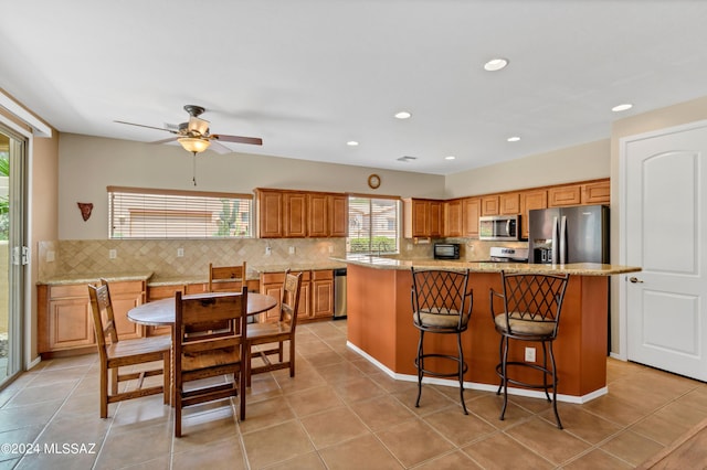 kitchen featuring stainless steel appliances, a center island, tasteful backsplash, brown cabinets, and ceiling fan