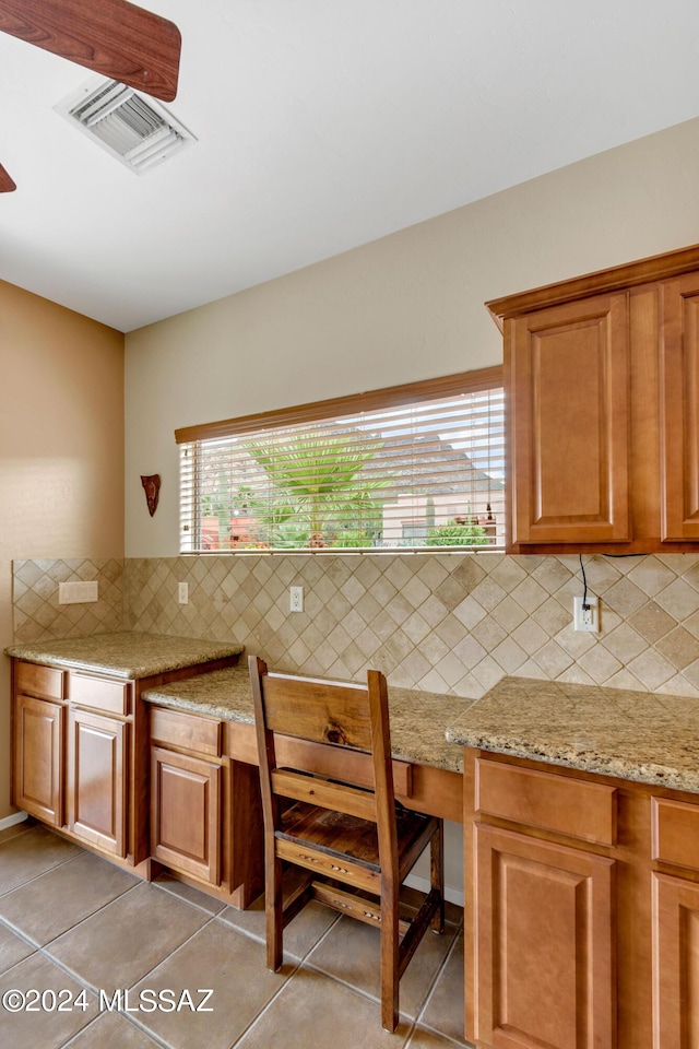kitchen with light tile patterned flooring, visible vents, backsplash, brown cabinets, and light stone countertops