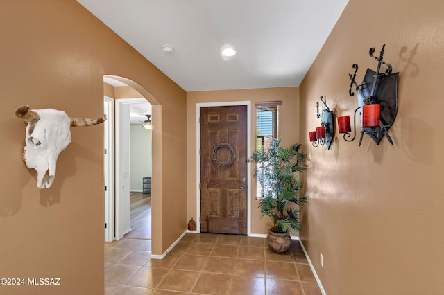 entryway featuring a ceiling fan, arched walkways, light tile patterned flooring, and baseboards