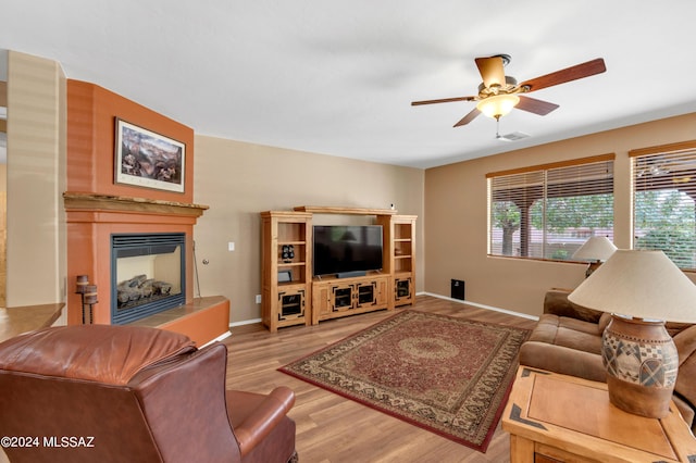living room featuring a fireplace with raised hearth, wood finished floors, visible vents, baseboards, and ceiling fan