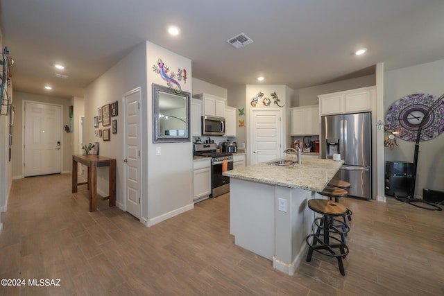 kitchen featuring white cabinetry, a center island with sink, light stone countertops, and appliances with stainless steel finishes