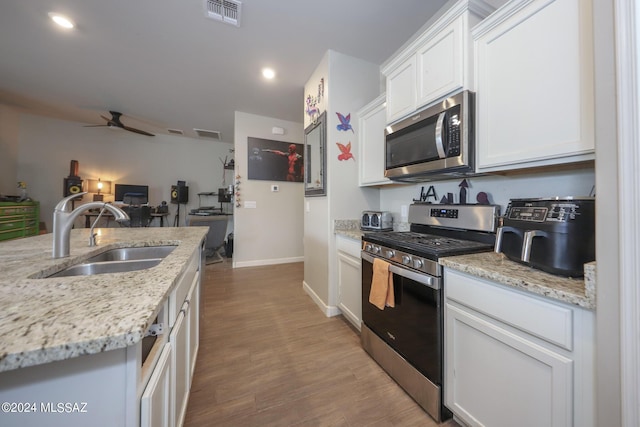 kitchen with sink, white cabinetry, light stone counters, appliances with stainless steel finishes, and light hardwood / wood-style floors