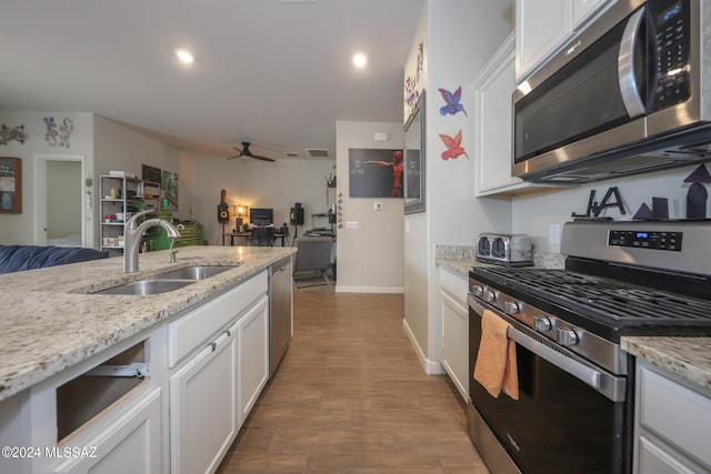 kitchen featuring sink, appliances with stainless steel finishes, hardwood / wood-style floors, light stone countertops, and white cabinets