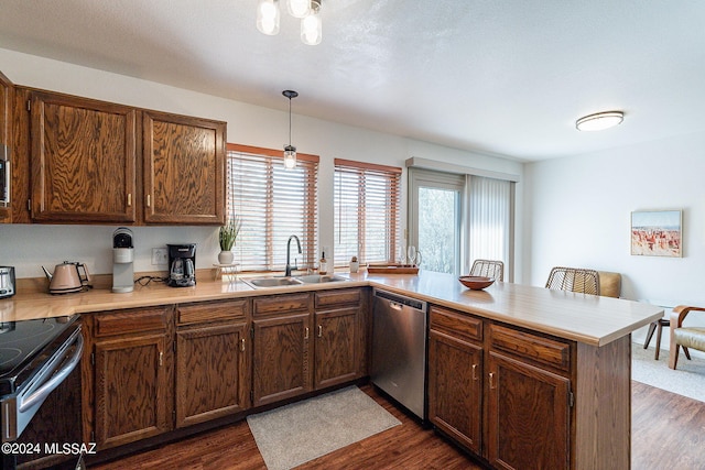 kitchen with dark wood-type flooring, hanging light fixtures, kitchen peninsula, stainless steel appliances, and sink