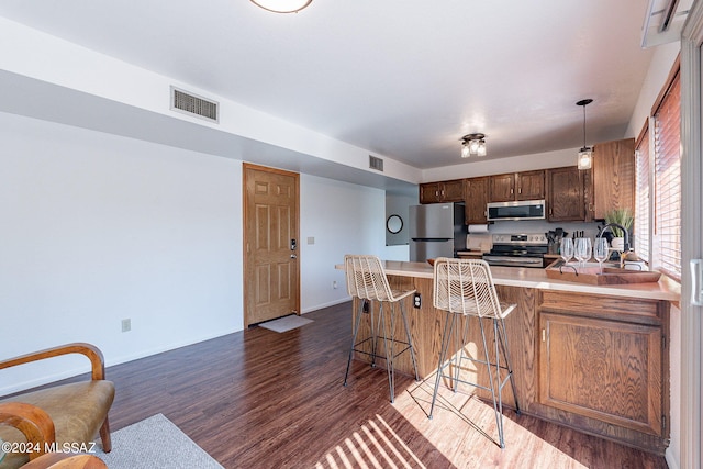 kitchen featuring dark hardwood / wood-style floors, kitchen peninsula, stainless steel appliances, a kitchen bar, and pendant lighting