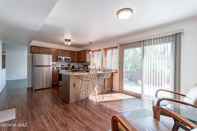 kitchen with dark hardwood / wood-style flooring, kitchen peninsula, stainless steel appliances, pendant lighting, and a breakfast bar