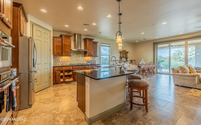 kitchen with visible vents, brown cabinets, stainless steel appliances, wall chimney exhaust hood, and a sink