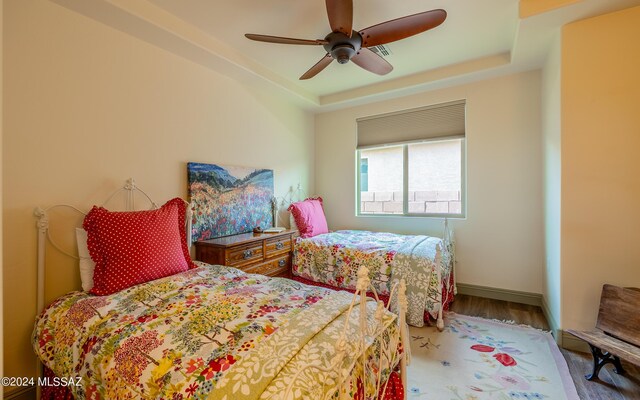 bedroom with ceiling fan, a tray ceiling, and hardwood / wood-style floors