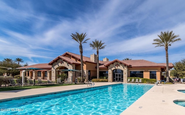 pool with a patio area, a community hot tub, and fence