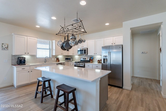 kitchen with sink, white cabinetry, stainless steel appliances, a center island, and light wood-type flooring