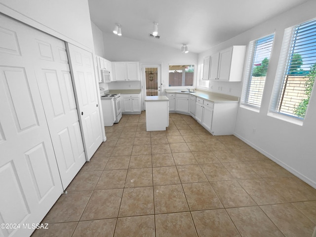 kitchen featuring white appliances, white cabinetry, a center island, light tile patterned floors, and vaulted ceiling