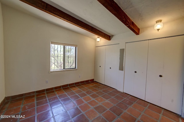 unfurnished bedroom with tile patterned floors, two closets, and beamed ceiling