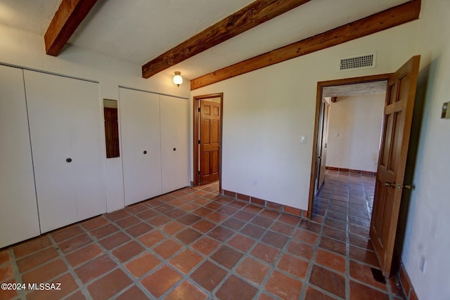 unfurnished bedroom featuring vaulted ceiling with beams, two closets, and tile patterned flooring