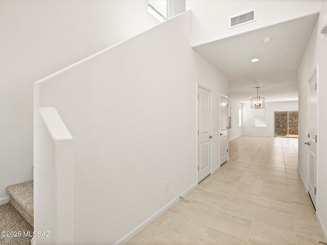 hall featuring visible vents, baseboards, a notable chandelier, and stairway